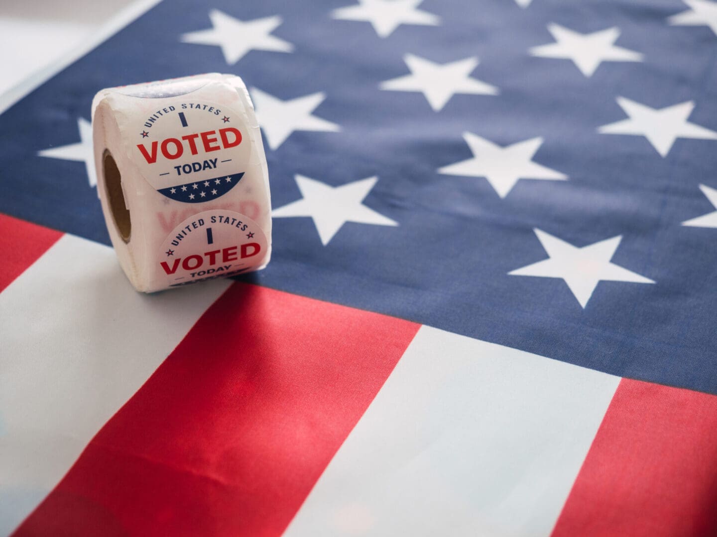 A roll of voting paper sitting on top of an american flag.